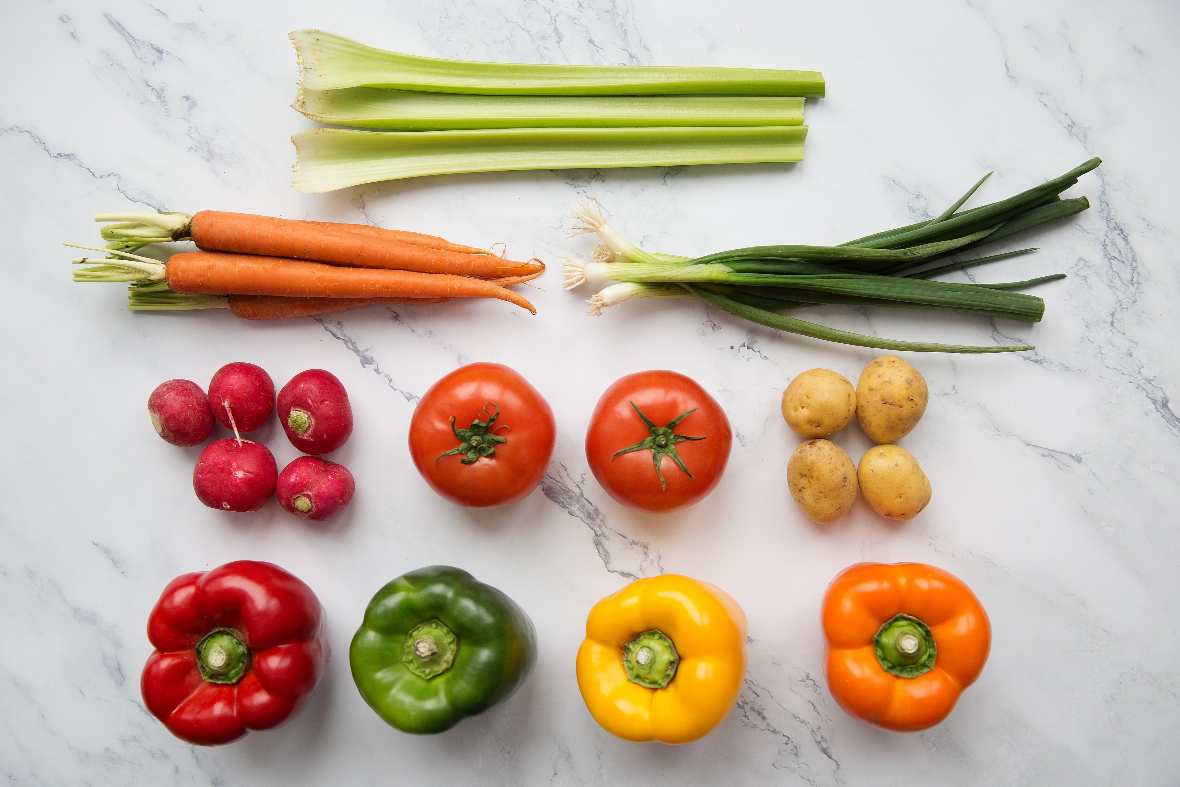 celery, carrots, scallions, radishes, tomatoes, mushrooms, and sweet peppers on a marble cutting board